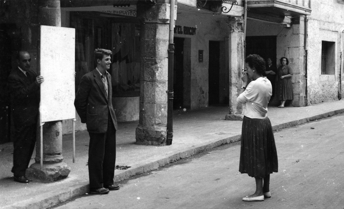 Piedad prepara un retrato en la calle. Un hombre posa ante un fondo blanco sostenido por otra persona.